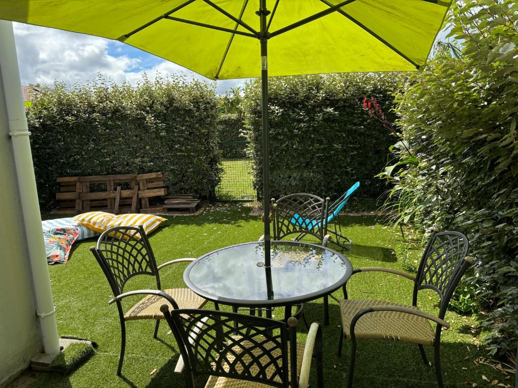 une table et des chaises sous un parapluie jaune dans l'établissement Appartement au calme à 10min des plages - avec Rez de Jardin et Terrasse, à Bénesse-Maremne