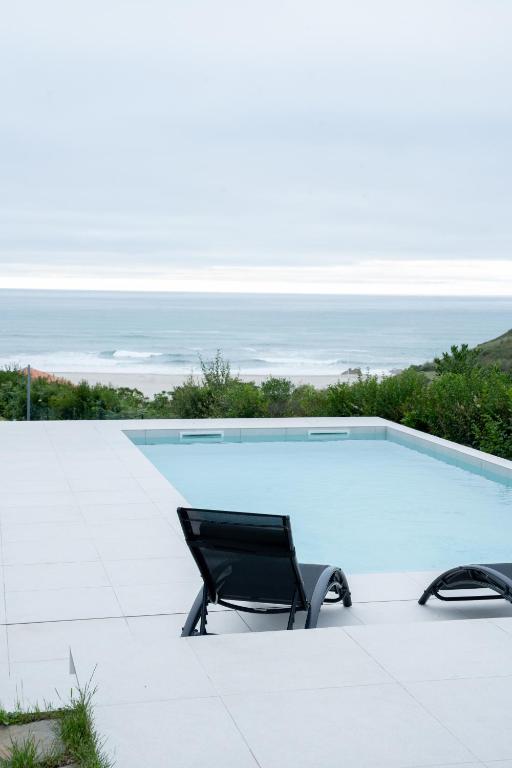 a swimming pool with a chair and the ocean at Balcobo Villas&Cabañas in A Coruña