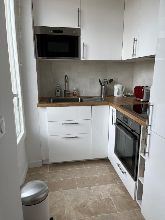 une petite cuisine avec des armoires blanches et un évier dans l'établissement Chez Luna - Stade de France - Paris, à Saint-Denis