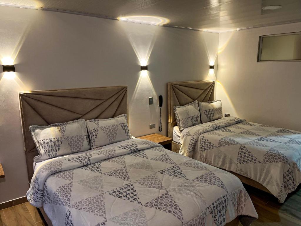 ボゴタにあるHotel Casa Baqueroのベッドルーム1室(ベッド2台付)、壁に照明が備わります。