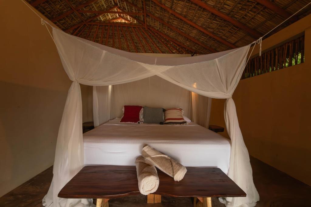 Una cama con dosel con dos bancos en una habitación. en Cabanas Adobe Frente Al Mar, en Puerto Escondido