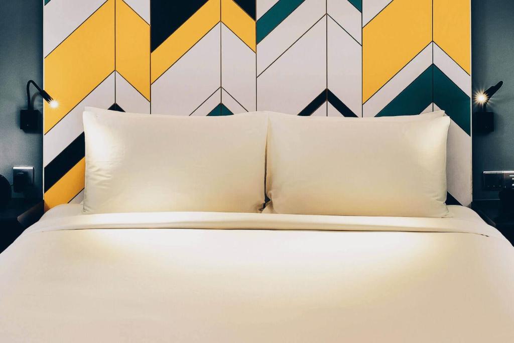 a white bed with two pillows and a colorful wall at The Kuala Lumpur Journal Hotel in Kuala Lumpur