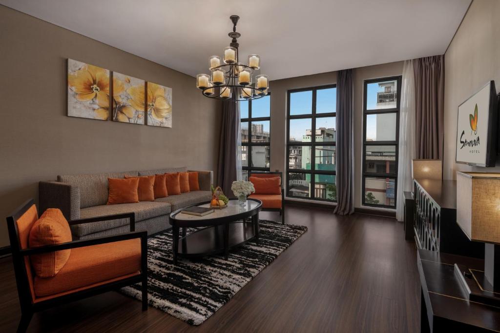 A living room with a sofa, armchairs, television and broad city-facing windows.