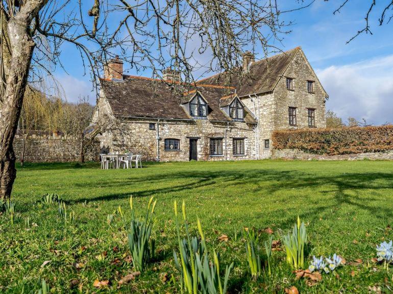 an old stone house on a field with a tree at Cosy & historic 2 bedroom Elizabethan cottage in Abergavenny