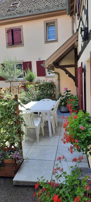 d'une terrasse avec une table blanche, des chaises et des fleurs. dans l'établissement Le Repaire des Hirondelles - Le Colombage, à Scharrachbergheim-Irmstett