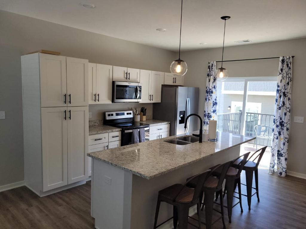 a kitchen with white cabinets and a island with bar stools at The Cottonwood at Coventry Rows in Omaha