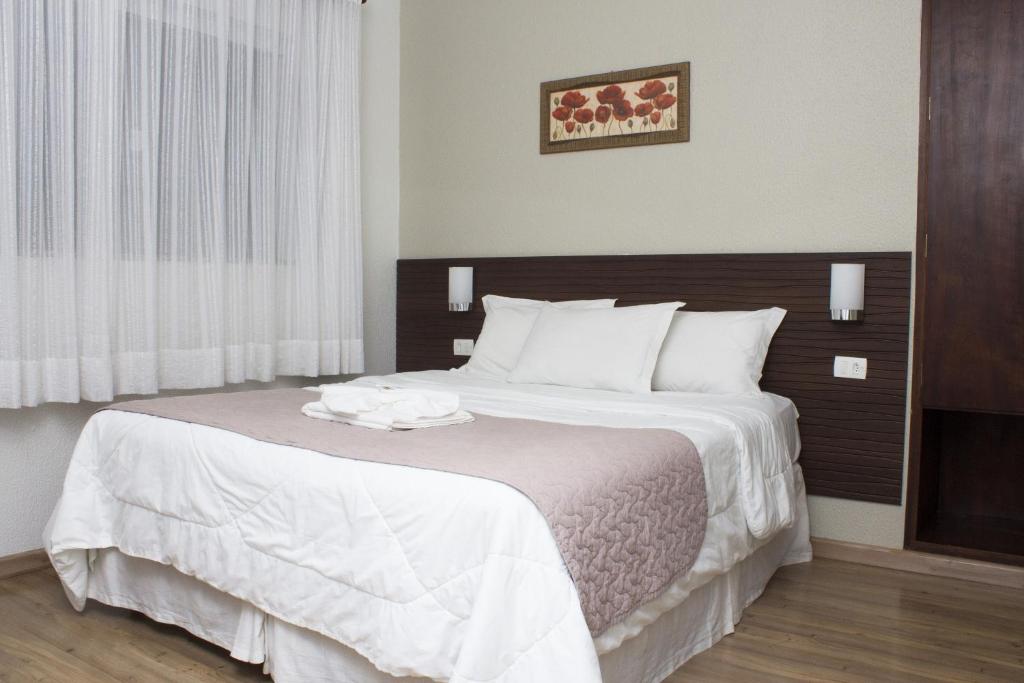 um quarto com uma cama grande e lençóis brancos em Hotel Nelo em Jaraguá do Sul