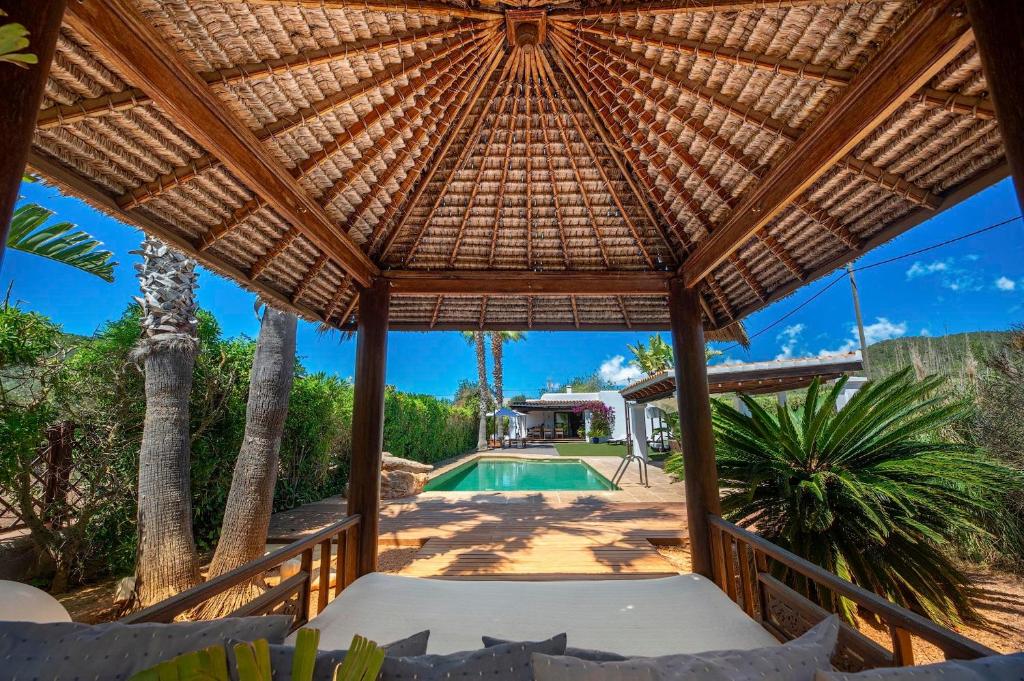 an outdoor patio with a wooden umbrella and a swimming pool at Can Botanic in Sant Josep de sa Talaia