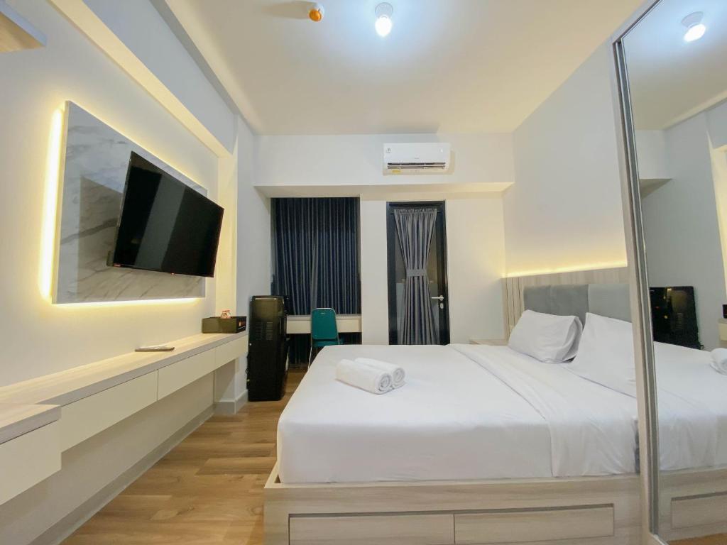 a bedroom with a white bed and a flat screen tv at Fully Furnished 1BR The Alton Apartment By Travelio in Semarang