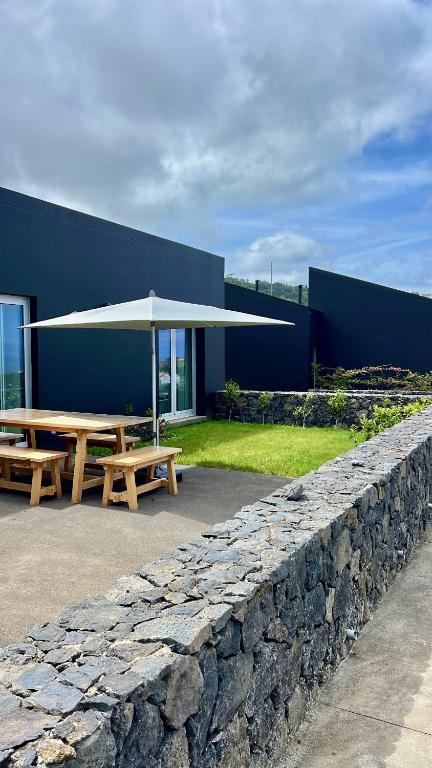 a picnic table with an umbrella next to a stone wall at Casas da Prainha B in Santo Amaro