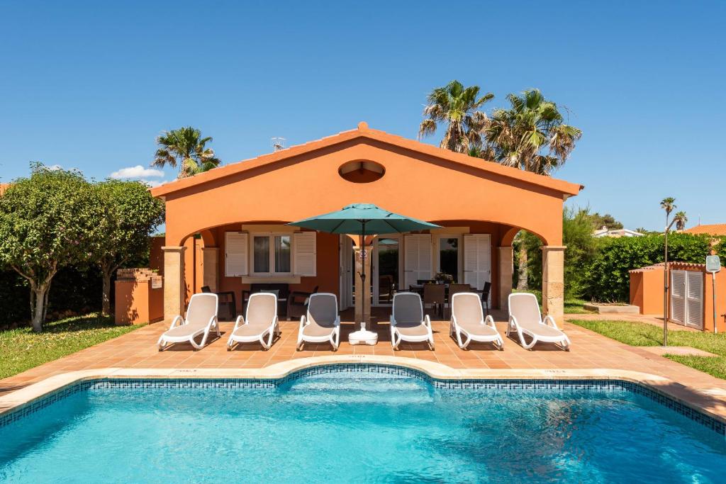 a house with a swimming pool with chairs and an umbrella at Villas Begonias in Cala'n Bosch