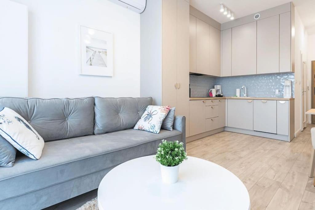 a living room with a gray couch and a kitchen at VacationClub - Moon Residence Apartament 14 in Ustronie Morskie