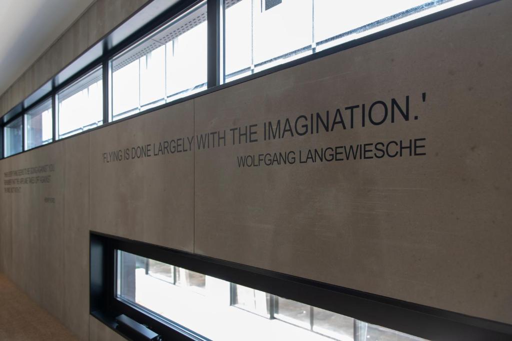 An interior wall displays a large Wolfgang Langewiesche quotation beside tall windows.