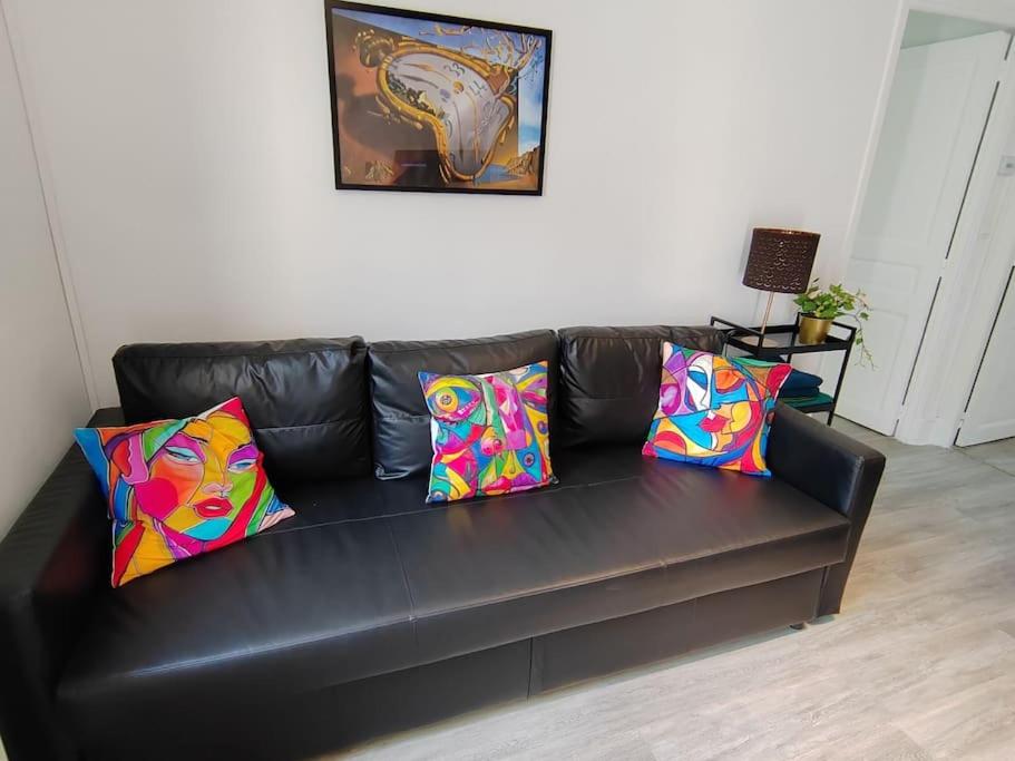 - un canapé en cuir noir avec 4 oreillers colorés dans l'établissement Le Surréaliste près de Nancy, à Varangéville