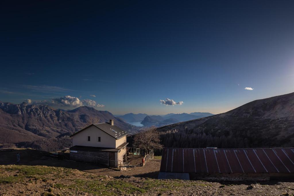 una piccola casa su una collina con montagne sullo sfondo di Agriturismo Alpe Rompiago a Bidogno