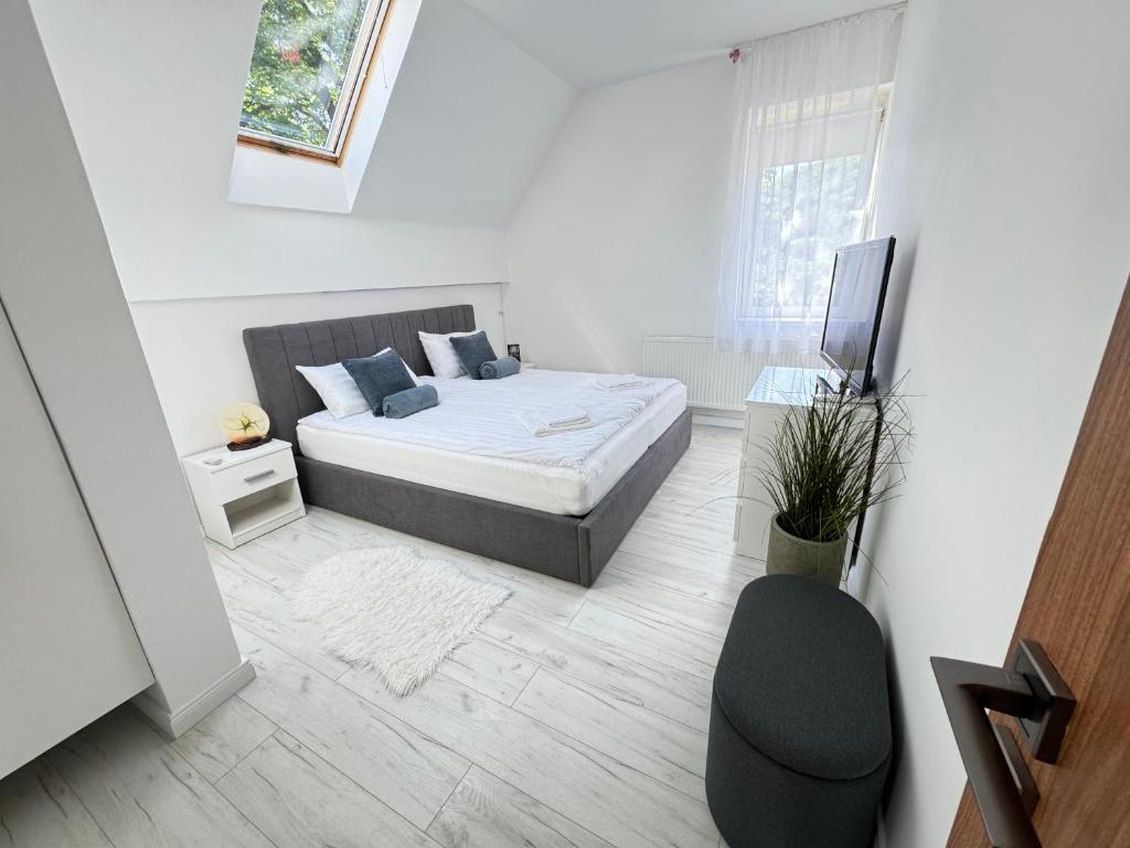a white bedroom with a bed and a chair at tettyeapartman in Pécs