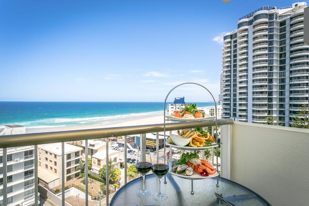 a balcony with a table with wine glasses and the ocean at Surfers Beachside Holiday Apartments in Gold Coast