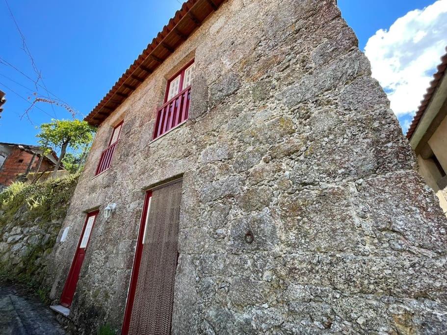a stone building with red windows and a brick wall at Casa dos Cabencos in Terras de Bouro