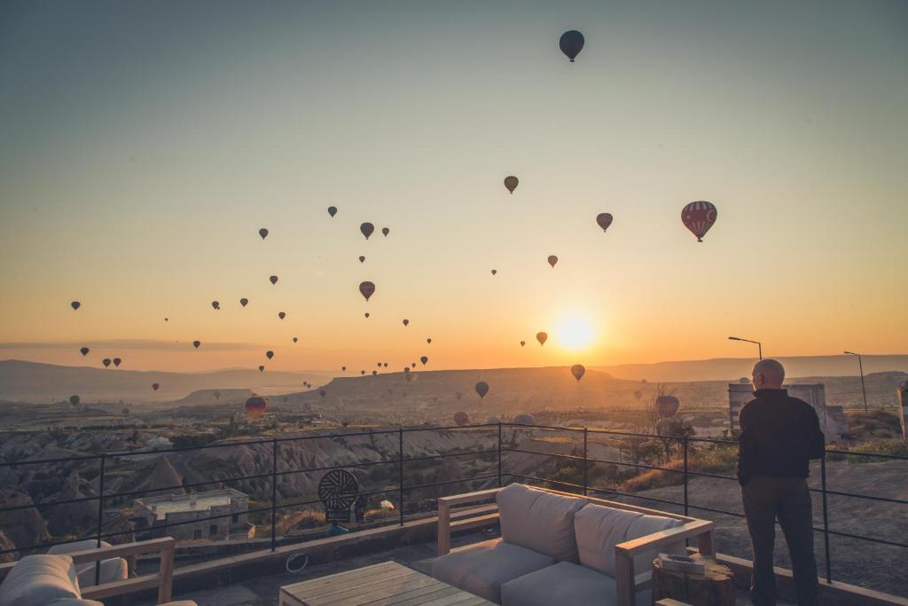 un homme debout sur un balcon qui regarde des montgolfières dans l'établissement Millstone Cave Suites Hotel, à Uçhisar