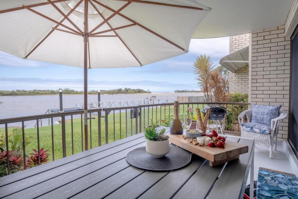 eine Holzterrasse mit Sonnenschirm und einem Tisch mit Obst in der Unterkunft Peaceful River Front Escape Short walk to Ocean St in Maroochydore