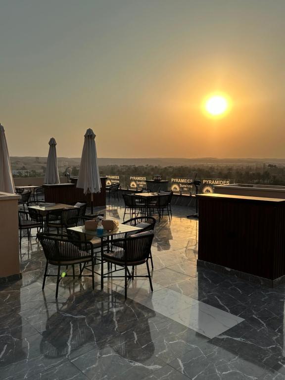 un patio con mesas y sillas con la puesta de sol en el fondo en Pyramids Sunshine Hotel, en El Cairo