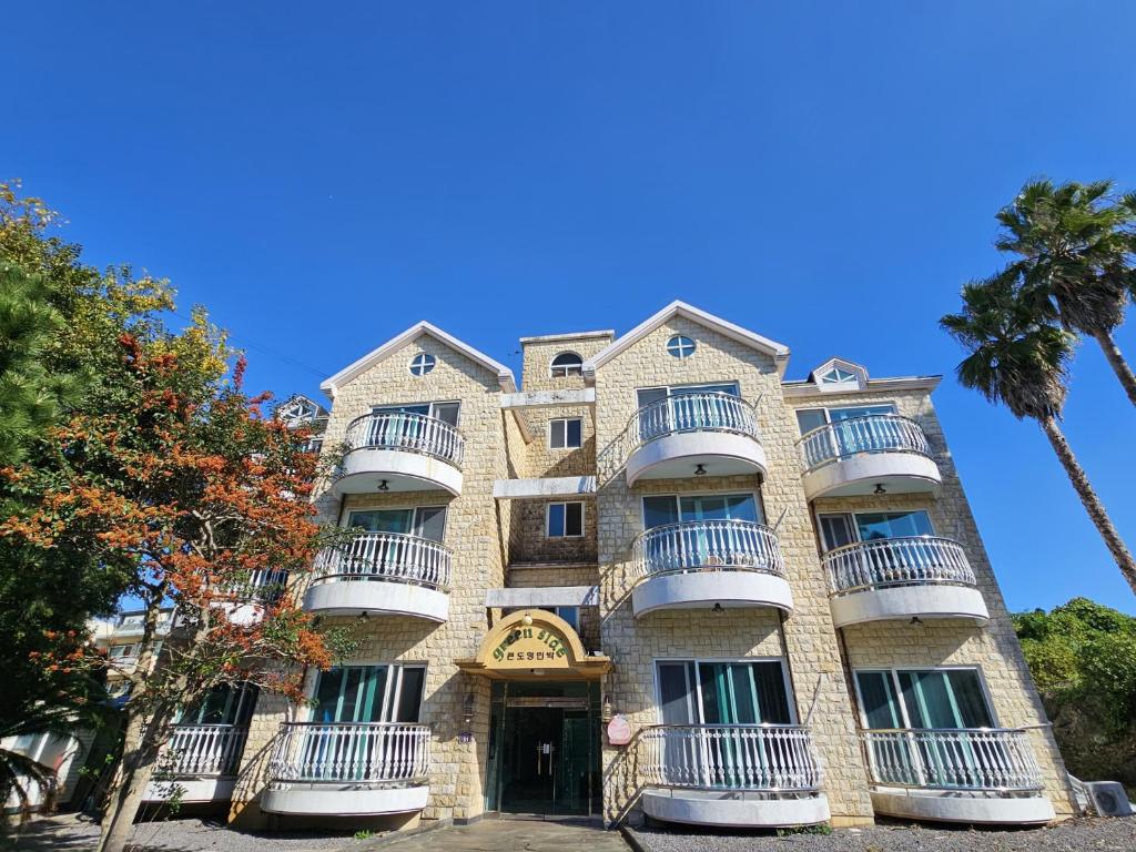 an apartment building with balconies and a palm tree at Greenside Pension in Seogwipo
