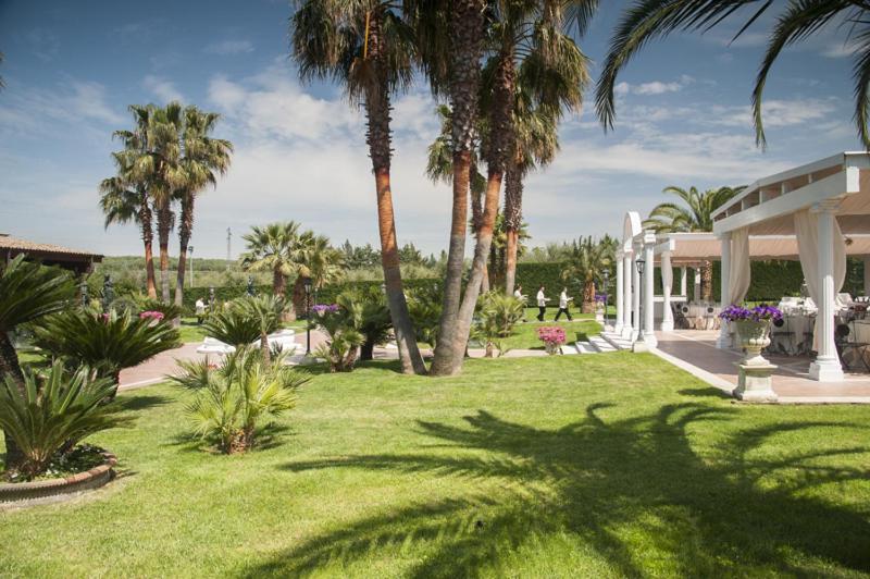 un parque con palmeras y un edificio blanco en La Corte di Opaka, en Canosa di Puglia