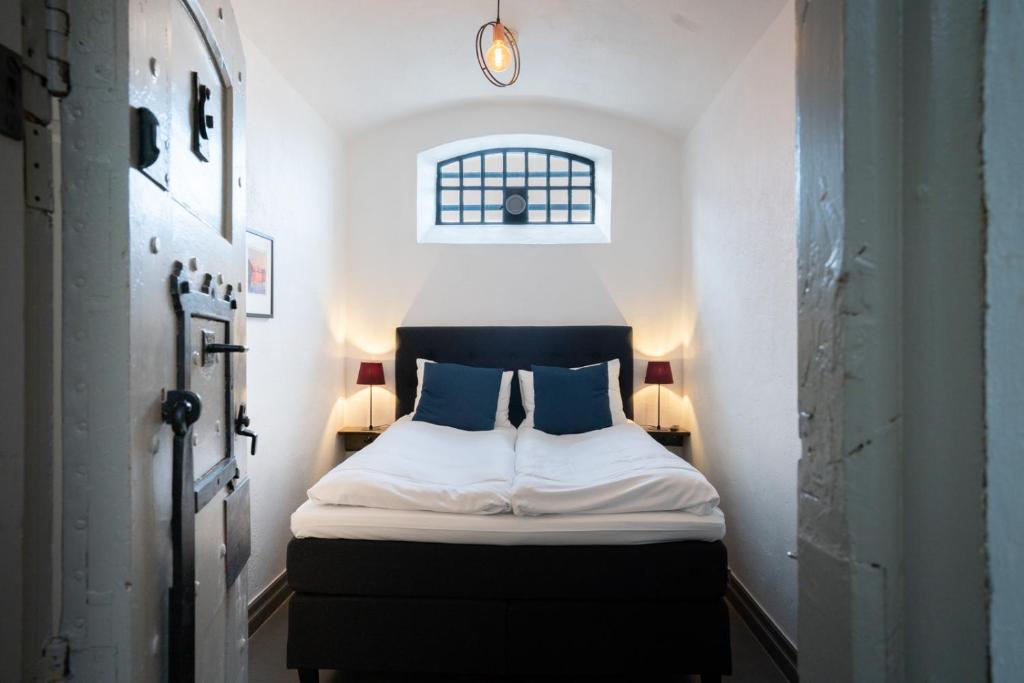 ein kleines Schlafzimmer mit einem Bett mit zwei blauen Kissen in der Unterkunft Gamle Fengselet Kulturhotell in Stord