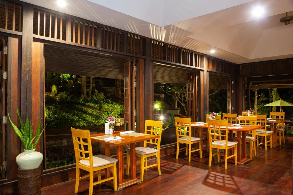 a restaurant with wooden tables and yellow chairs at Baan Krating Phuket Resort -SHA Plus in Nai Harn Beach