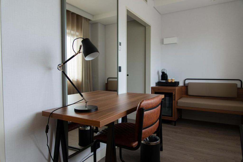 A compact wooden desk with an adjustable lamp sits beside a lounge bench and minibar.
