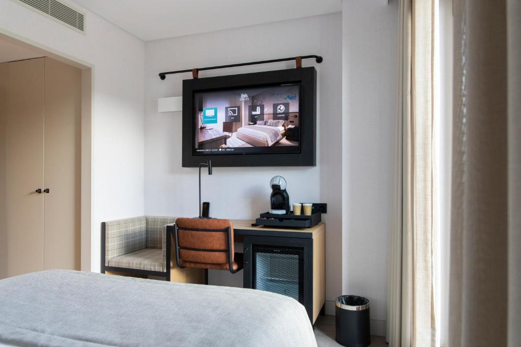 A compact room corner with wall-mounted TV, desk, beverage station, and upholstered chair.