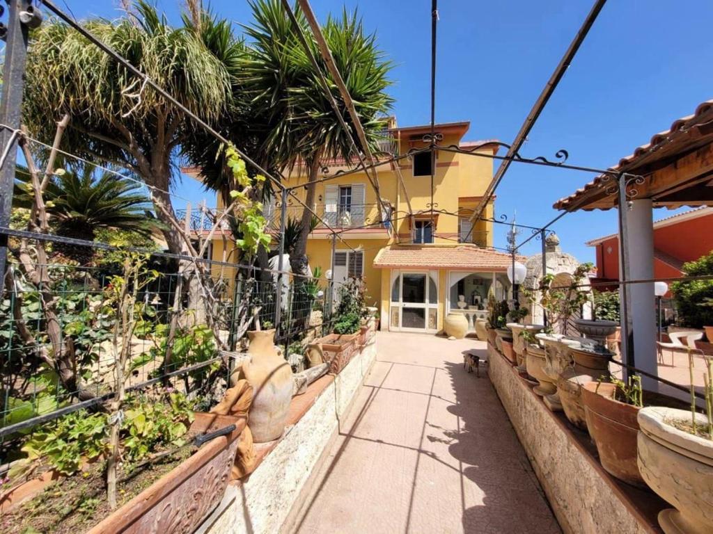 a yellow house with palm trees and a sidewalk at La casa di Sonia in Fanusa