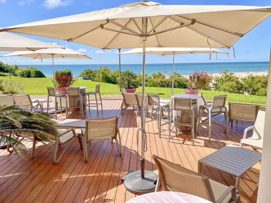 a deck with tables and chairs and an umbrella at Hôtel Miléade La Frégate - Bidart in Bidart