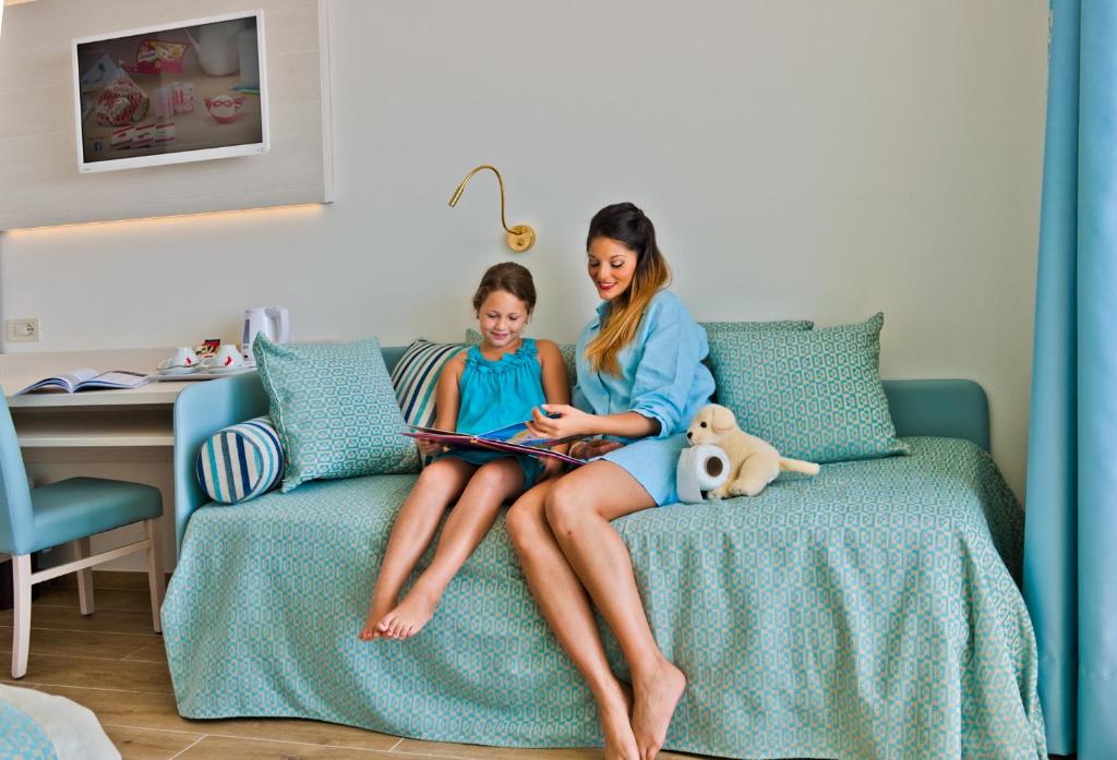 two girls sitting on a bed looking at a tablet at Hotel Montecarlo in Bibione