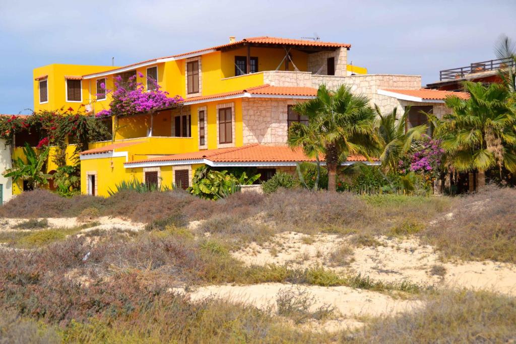 a yellow house on the beach with palm trees at Guest House Orquidea in Sal Rei