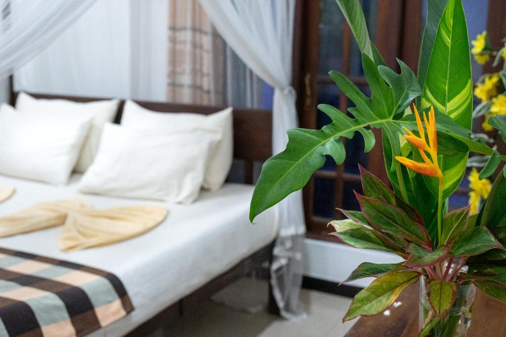 ein Bett mit weißen Kissen und einer Pflanze in einem Zimmer in der Unterkunft Villa Sunimal in Unawatuna
