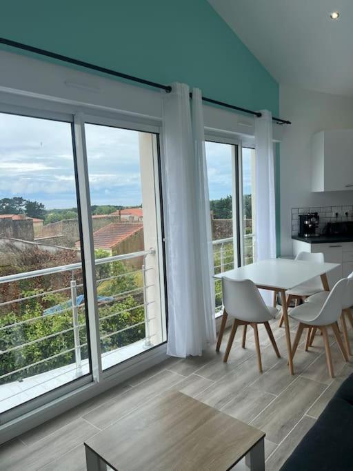 - un salon avec une table, des chaises et de grandes fenêtres dans l'établissement Maison Centre Brem avec vue sur la côte, à Brem-sur-Mer