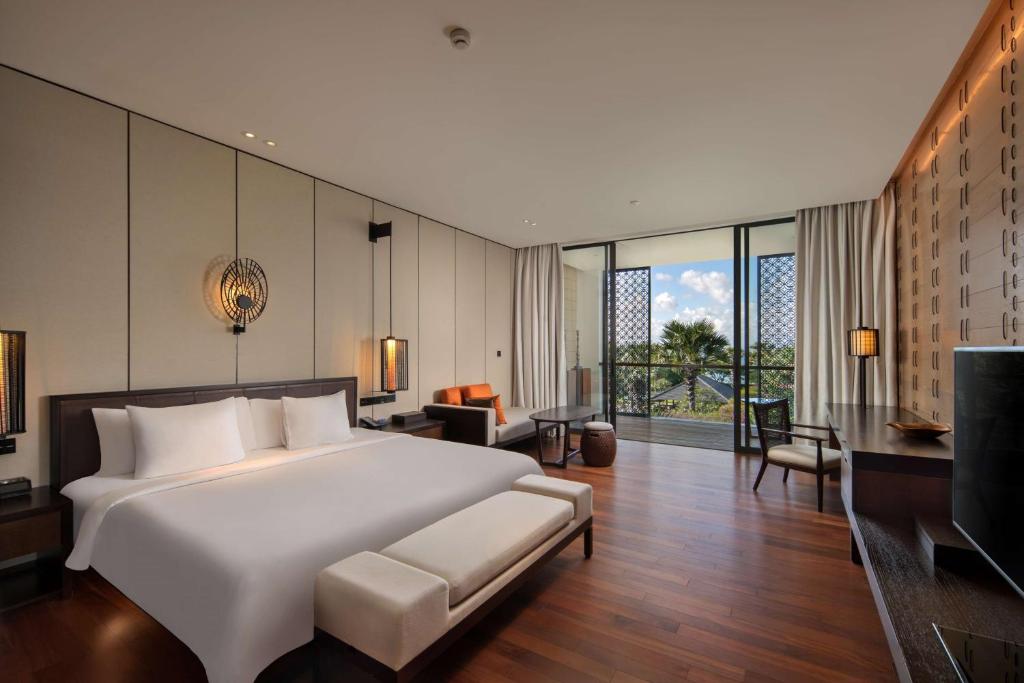 a bedroom with a large white bed and a living room at Radisson Blu Bali Uluwatu in Uluwatu