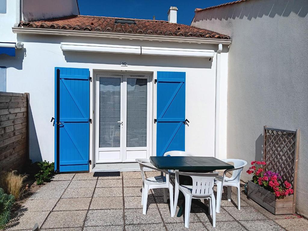 une table et des chaises à l'extérieur d'une maison avec portes bleues dans l'établissement Charmante Maisonnette à 200m de la Plage avec Jardin et Parking Privé - FR-1-476-9, à La Faute-sur-Mer