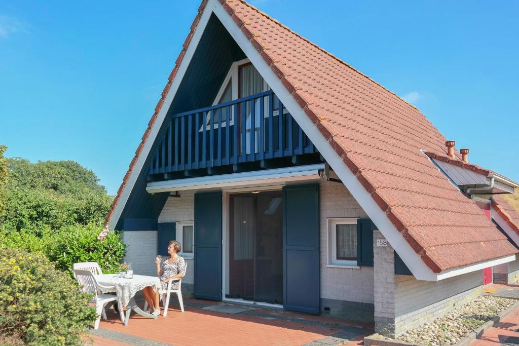 une femme assise à une table devant une maison dans l'établissement Dike House Affordable 6-Person Holiday Home Near the Sea Dike, à Anjum