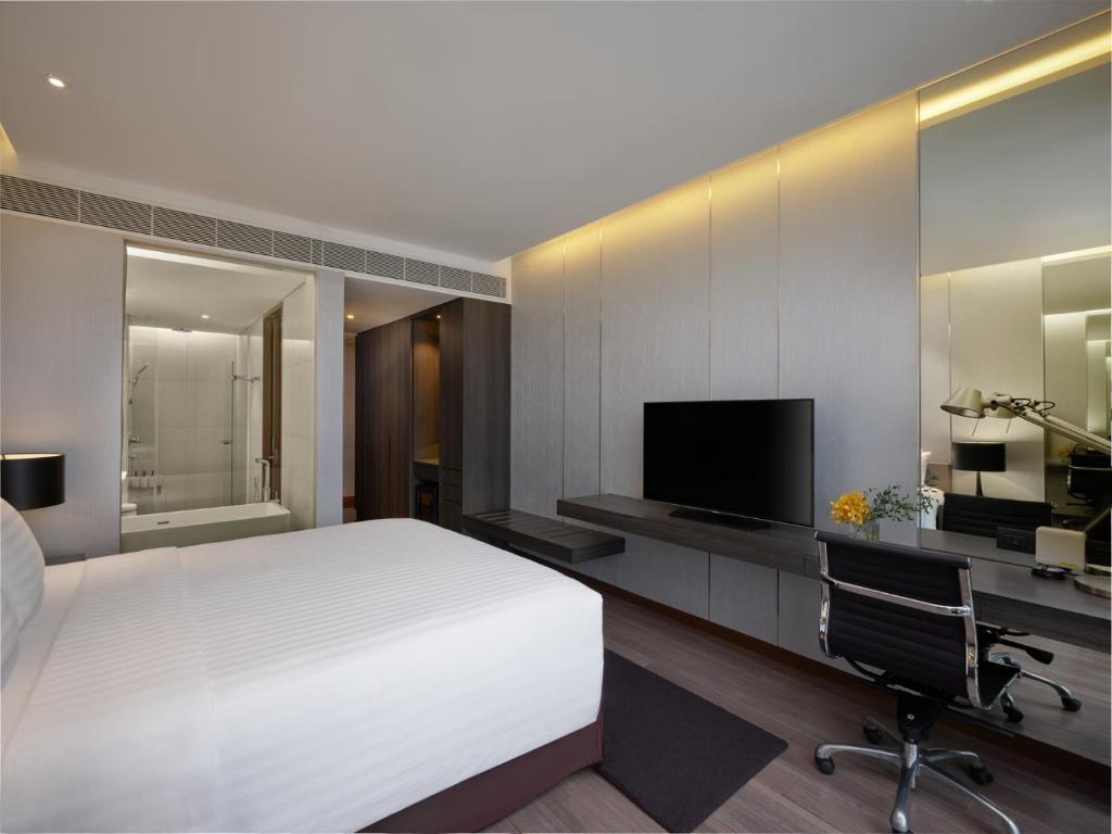 A bedroom with a built-in work desk, television console and glazed bathroom entrance.