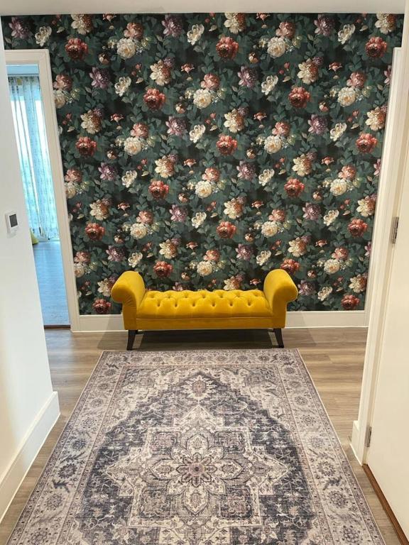 a yellow couch in a living room with a floral wallpaper at Healum Retreat - 3BR Apartment Southall in Southall