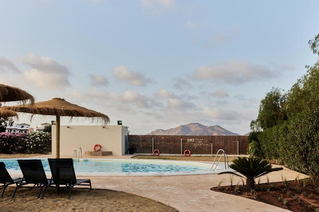 a resort pool with chairs and a mountain in the background at TAIGA Almeria Playa in Palomares