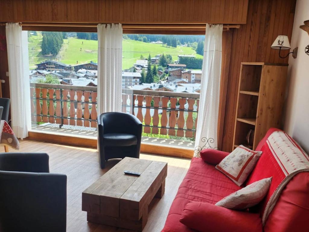 - un salon avec un canapé rouge et une grande fenêtre dans l'établissement Appartement 4 pièces pour 8 pers. avec garage, proche commerces et remontées mécaniques - FR-1-802-57, aux Gets