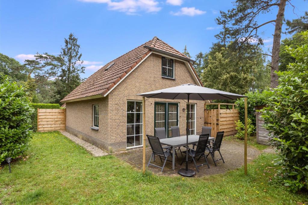 a table with an umbrella in front of a house at Comfortabel vakantiehuis in het bos op de Veluwe in Lunteren