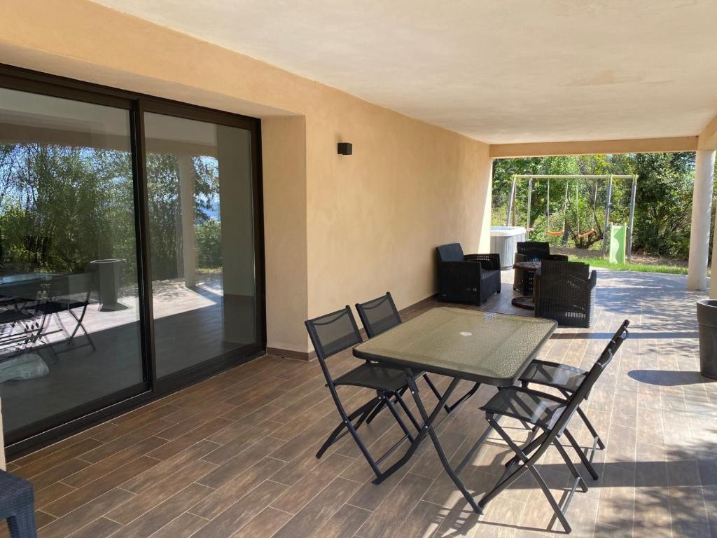 un patio con mesa, sillas y puertas de cristal en Bas de villa - Canella, en Sari Solenzara