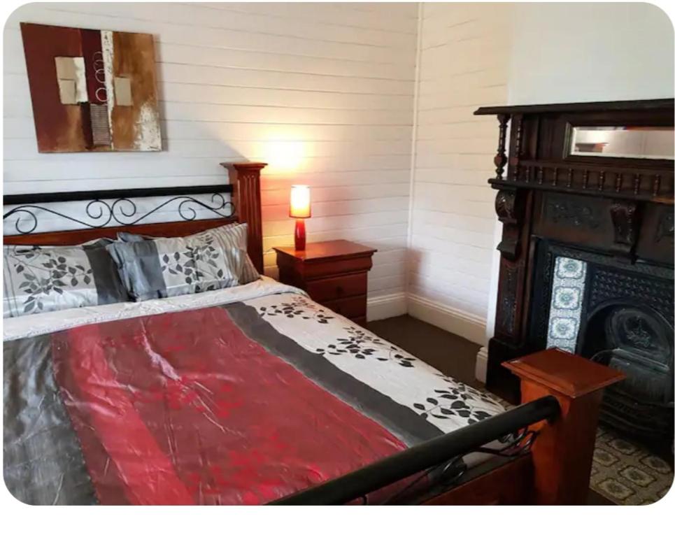 a bedroom with a bed with a red comforter and a fireplace at 4 Bedroom Federation Cottage in Lithgow