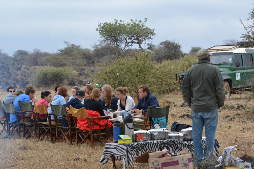 a group of people sitting at a table in a field at Maasai Simba Camp in Amboseli