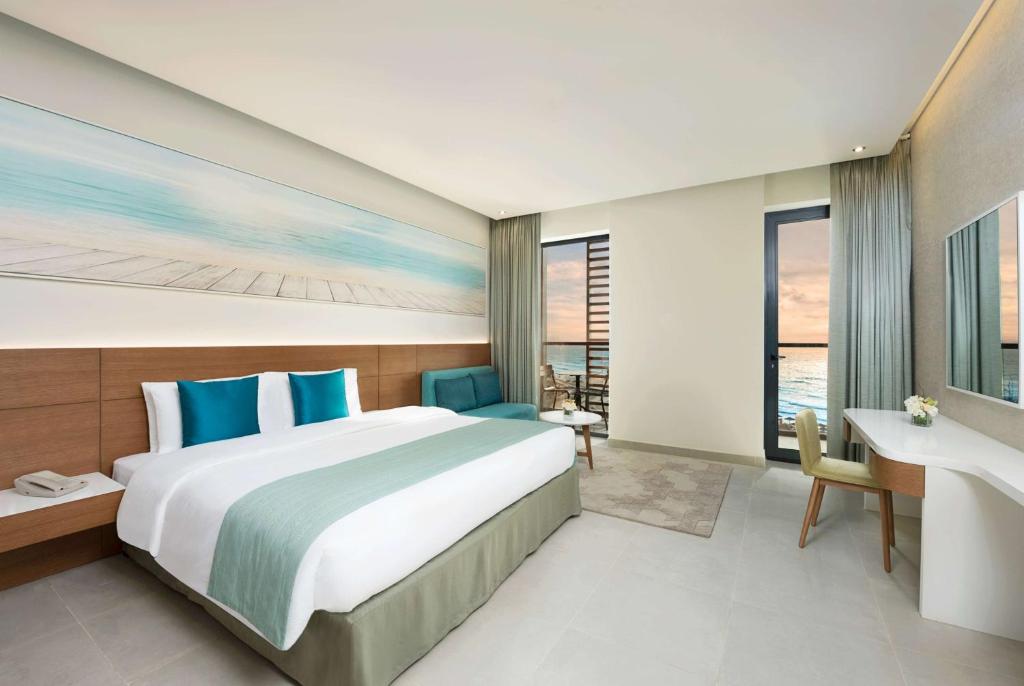 a bedroom with a large bed and a desk at Wyndham Garden Ajman Corniche in Ajman 
