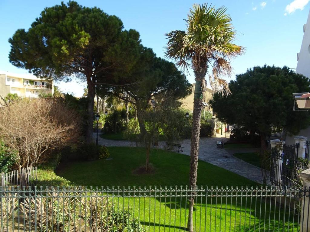 une clôture devant une cour avec un palmier dans l'établissement T2 climatisé au centre de Palavas, proche plage - FR-1-559-19, à Palavas-les-Flots
